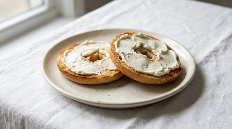 Plain bagel with cream cheese on a white ceramic plate with natural morning light