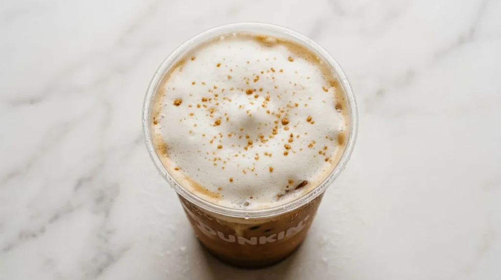 Close-up top view of Dunkin Cookie Butter cold foam showing its airy cloud-like texture with cookie crumble specks